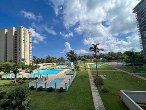 A hotel with a swimming pool, palm trees, and a clear sky. - Beachfront 2-Bedroom Apartment with Resort-Style Amenities in Luquillo (Luquillo)