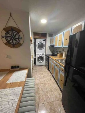 A compact kitchen with a washing machine, a refrigerator, and a dining area with a bench. - Beachfront 2-Bedroom Apartment with Resort-Style Amenities in Luquillo (Luquillo)
