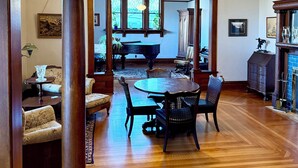 Un comedor amplio con una mesa y sillas de madera, una araña y vista a una cocina a través de una ventana.