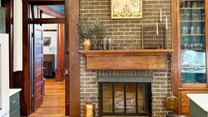 Una cocina con chimenea de ladrillo, piso de madera y vista al comedor.