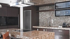 Een moderne keuken met granieten aanrechtbladen, roestvrijstalen apparatuur en een inbouwkookeiland met zitplaatsen.