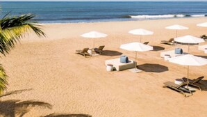 Een strand met witte parasols en ligbedden, palmbomen en de oceaan.