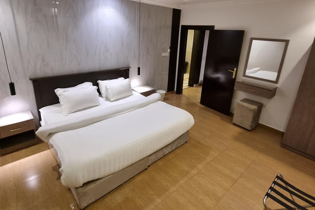 A modern hotel room with a large bed, bedside tables, a mirror, and a wardrobe.