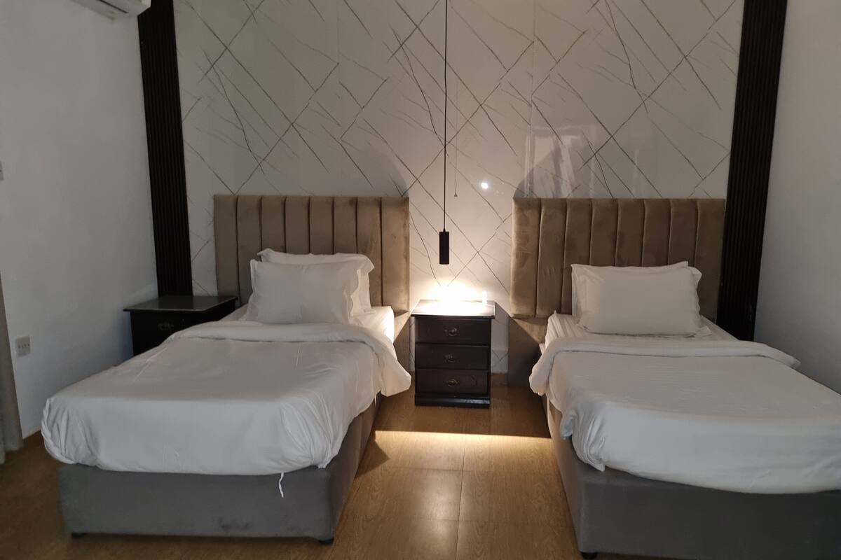 A twin bedroom with two beds, a nightstand, a dresser, and a pendant light.