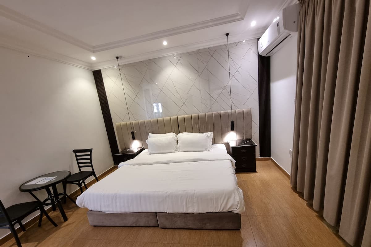 A modern hotel room with a large bed, bedside tables, a chair, and a small table.