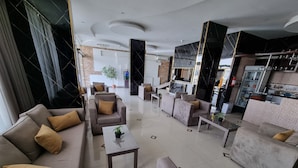 Een moderne hotellobby met banken, een salontafel en een keuken in de achtergrond.