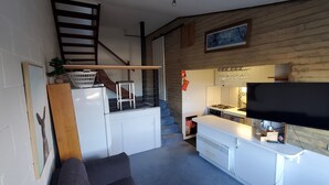 Um espaço de estar compacto com cozinha compacta, televisão de tela plana, escada e um pequeno espaço para sentar.