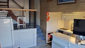 Sala moderna com sofá cinzento, escada, área de cozinha e uma obra de arte pendurada na parede.