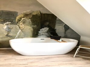 A modern bathroom with a freestanding bathtub, a small stool, and a mural on the wall. - Beautiful Lodge Located on the Church Square (Zoutelande)
