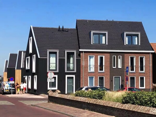 A row of modern houses with a mix of black and red brick facades, large windows, and a clear sky. - Beautiful Lodge Located on the Church Square (Zoutelande)