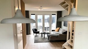 Ein modernes Wohnzimmer mit einer Couch, einem Couchtisch und Sesseln. Eine Treppe führt zu einer oberen Ebene mit einem Balkon.