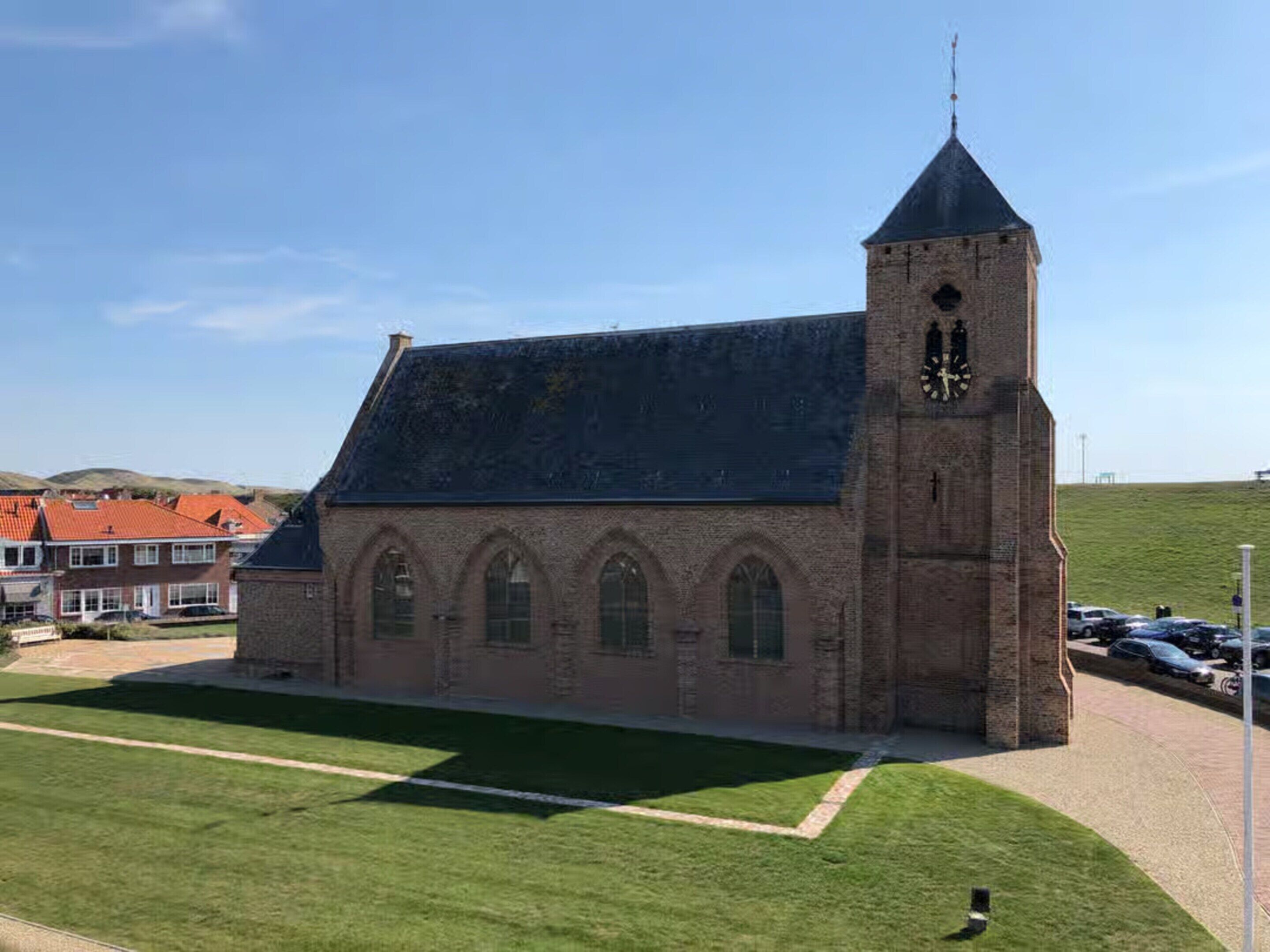 Eine Kirche mit hohem Turm und einer Uhr, umgeben von einer Rasenfläche und Wohnhäusern.