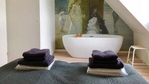Ein Zimmer mit einer großen Badewanne, einem kleinen Hocker und einem Gemälde an der Wand.