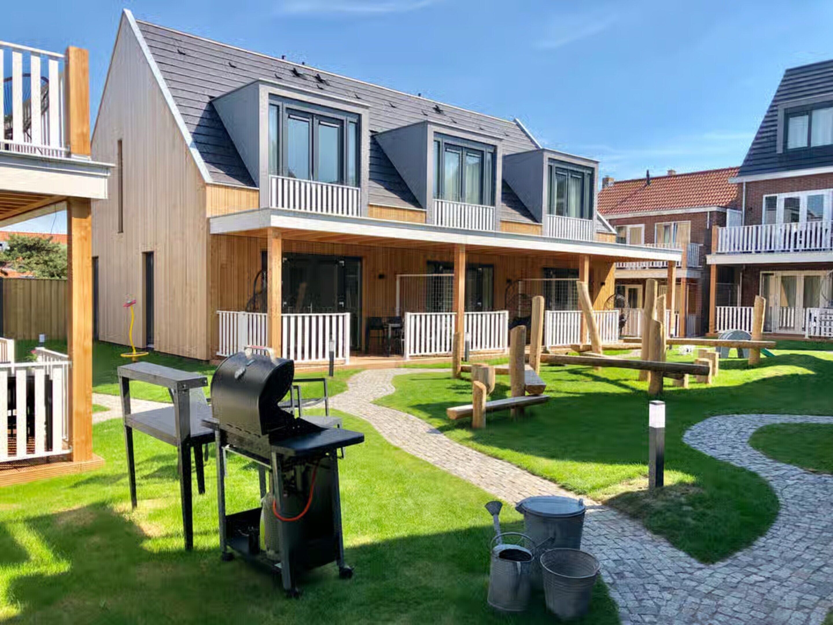 A modern residential building with a covered patio, outdoor seating, and a barbecue area.