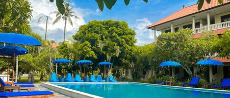 A swimming pool with blue umbrellas, lounge chairs, and a building with a red roof.