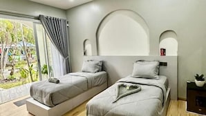 A modern bedroom with two beds, a large window with curtains, a curved ceiling, and a small table with a plant. - New Mekar Jaya Hotel (Kuta)