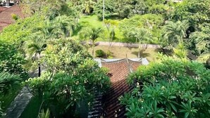 A lush garden with a pond, surrounded by tropical plants and a traditional building with a tiled roof. - New Mekar Jaya Hotel (Kuta)