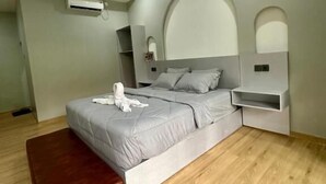 A modern bedroom with a bed, a wooden bench, an air conditioning unit, and built-in nightstands. - New Mekar Jaya Hotel (Kuta)