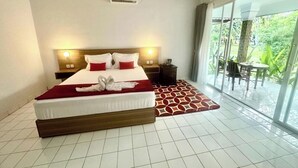 A hotel room with a large bed, a bedside table, a nightstand, a window with a view of greenery, and a sliding glass door to an outdoor area. - New Mekar Jaya Hotel (Kuta)