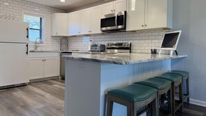 A modern kitchen with white cabinets, a central island with bar stools, a microwave, and a stove. - Forest Park – 2BR Pool, Clubhouse & Beaches (Englewood)