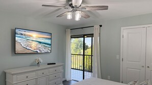 A bedroom with a bed, a dresser, a ceiling fan, a TV, and a balcony with curtains. - Forest Park – 2BR Pool, Clubhouse & Beaches (Englewood)