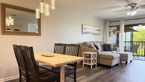 A dining area with a wooden table and chairs, a sofa, and a balcony with a view. - Forest Park – 2BR Pool, Clubhouse & Beaches (Englewood)