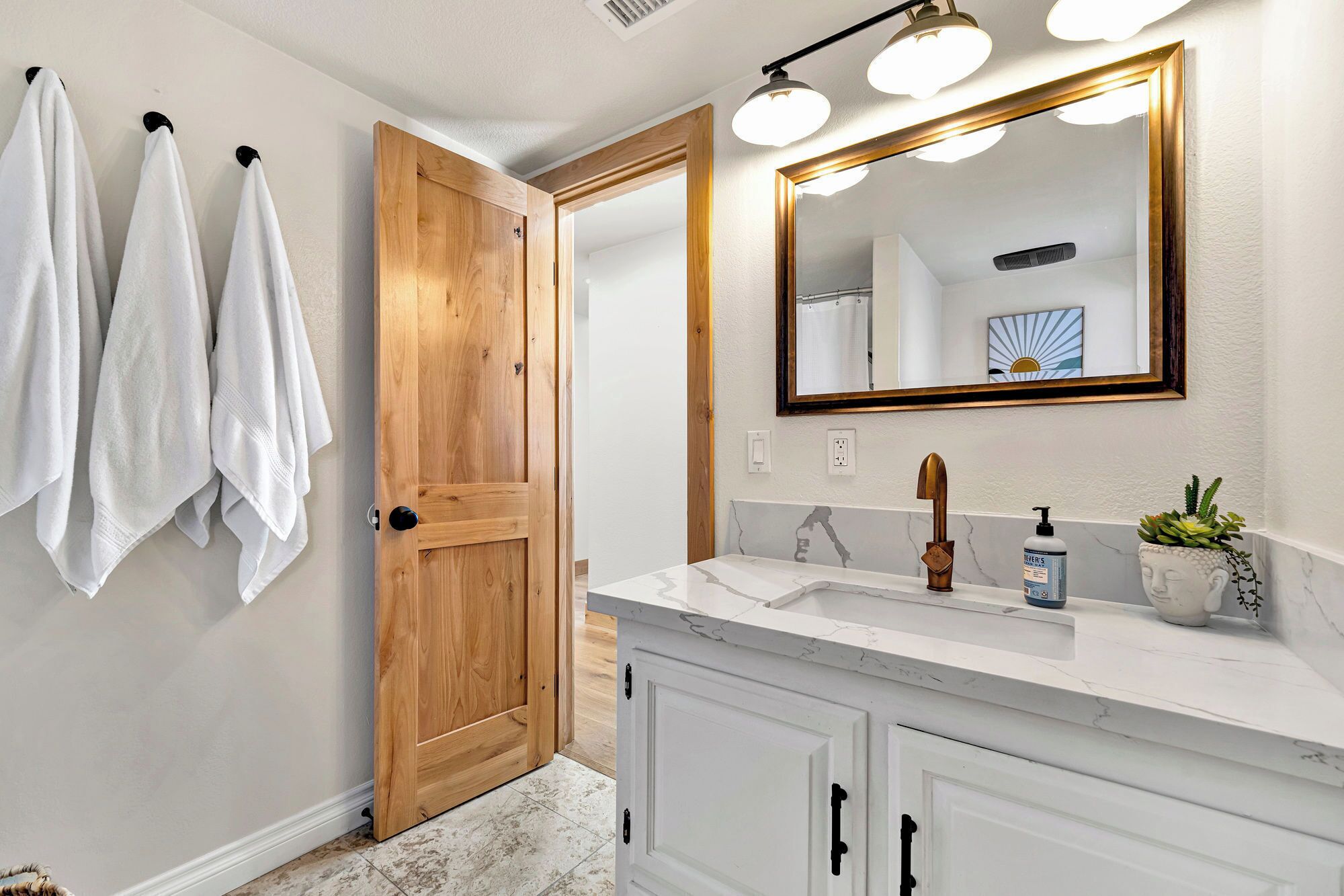 A bathroom with a wooden door, a white sink with a gold faucet, and a mirror with a gold frame.