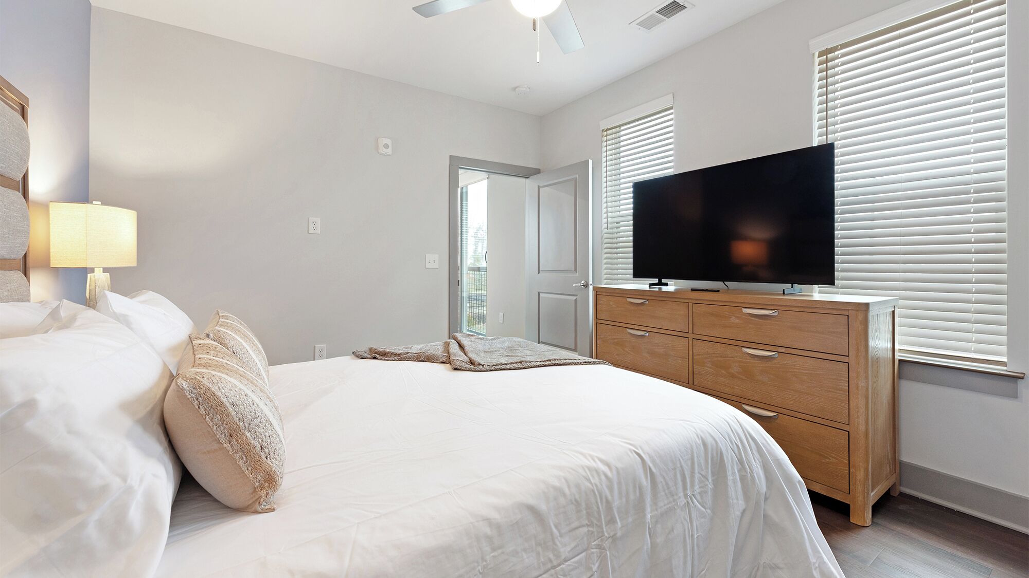 A bedroom with a bed, a TV on a wooden dresser, and a door leading to a balcony.