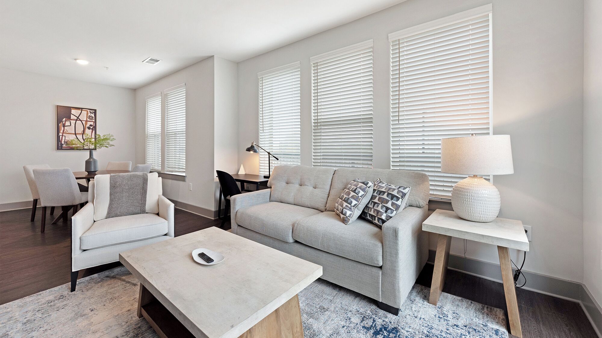 A modern living room with a sofa, armchairs, a coffee table, and a dining area with a table and chairs.