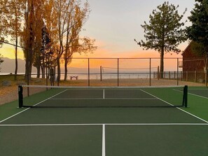 Tenniskenttä, jossa on verkko, ja jonka ympärillä on puita ja aita.