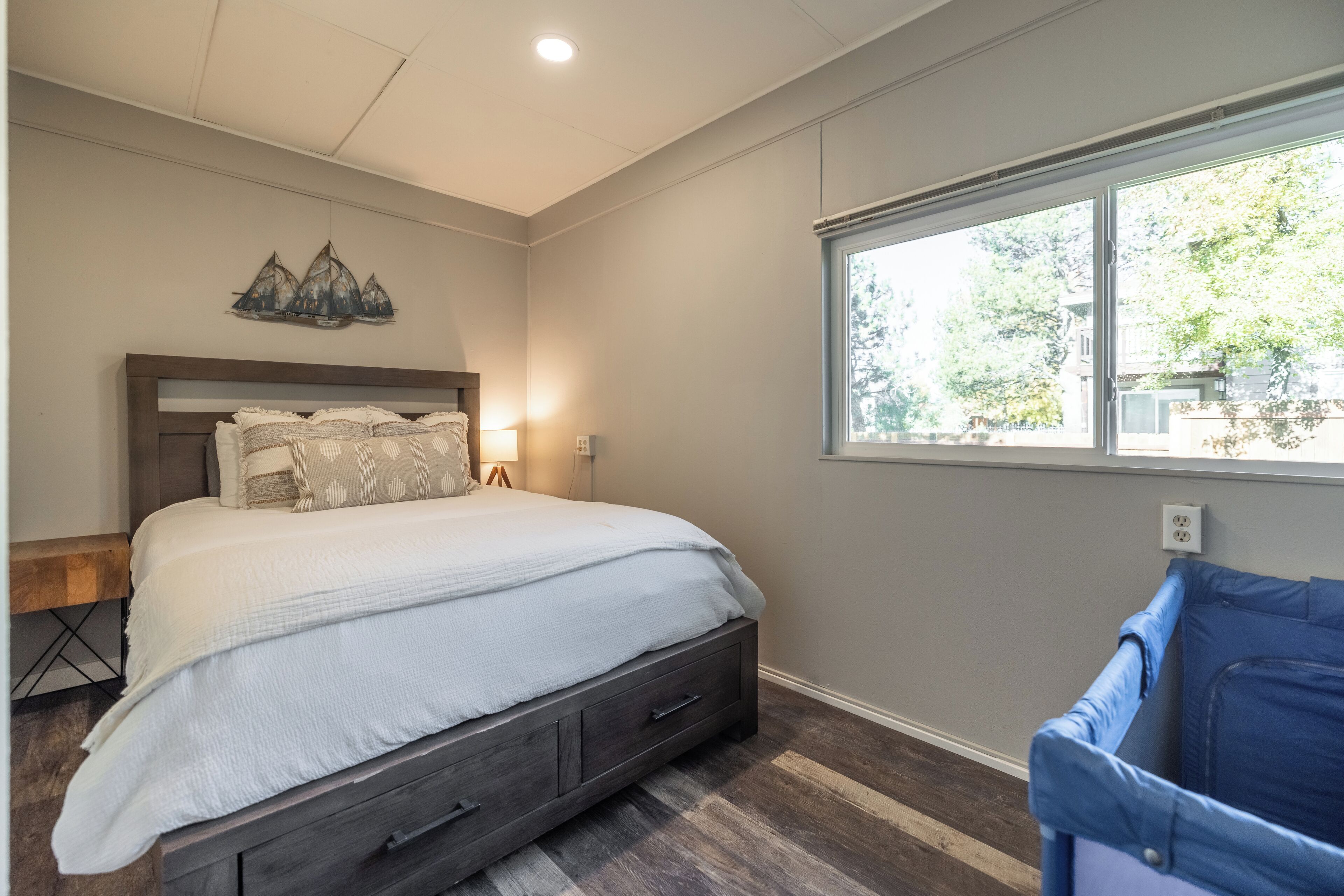 A bedroom with a bed, bedside table, lamp, and a window with a view of trees.