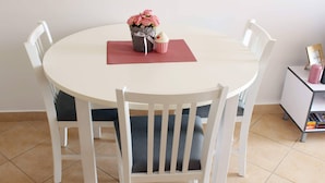 A round dining table with four white chairs, a vase with pink flowers, and a small pink candle on a side table. - Apartments Lovro - One Bedroom Apartment With Terrace and Sea View (Dubrovnik)