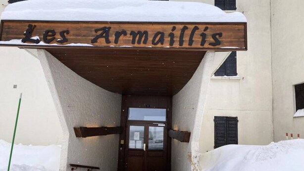 Een gebouw ingang met een houten bord met de tekst 'Les Armaillis' erboven.
