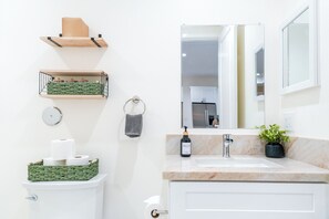 Een badkamer met een toilet, een wastafel met spiegel, een handdoekhouder en een groene mand op het toilet.