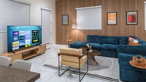 A modern living room with a flat-screen TV, a sofa, a coffee table, and a wooden accent wall. - Luxe Disneyland Multi-Family Villa • King Beds • Game Rooms • EV • Sleeps 28 (Santa Ana)