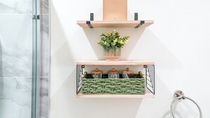 A bathroom with a glass shower enclosure, a towel rack, a shelf with a plant, and a woven basket. - Luxe Disneyland Multi-Family Villa • King Beds • Game Rooms • EV • Sleeps 28 (Santa Ana)