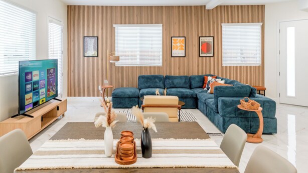 A modern living room with a sectional sofa, a flat-screen TV, and a wooden wall panel. - Luxe Disneyland Multi-Family Villa • King Beds • Game Rooms • EV • Sleeps 28 (Santa Ana)