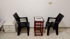 Een kleine kamer met twee zwarte plastic stoelen, een klein houten tafeltje en een witte ladekast.