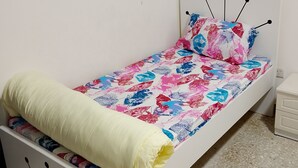Een kleine kamer met een enkel bed, een wit hoofdeinde en een kleurrijk bloemenbeddegoed.
