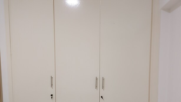 Een witte, gesloten garderobe met twee deuren en een handgreep op elke deur.