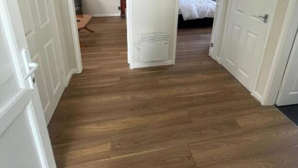 Un couloir avec un plancher en bois, des portes blanches et un radiateur.