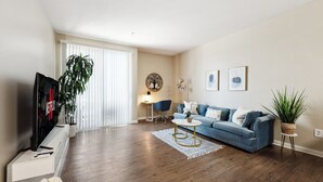 Ein modernes Wohnzimmer mit einem blauen Sofa, einem Couchtisch, einem Fernseher und einer Topfpflanze.
