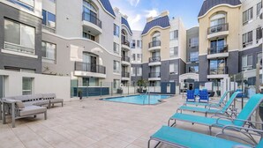 Ein moderner Apartmentkomplex mit Schwimmbad, Sitzgelegenheiten im Freien und Balkonen.