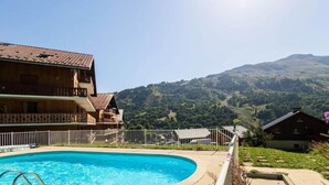 A pool area with a wooden building, a fenced deck, and a mountainous backdrop. - Apartment in Les Verneys Near Ski Lift (Valloire)