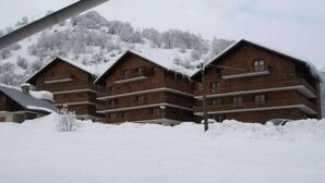 A row of wooden cabins with balconies, surrounded by snow-covered trees and a hill in the background. - Apartment in Les Verneys Near Ski Lift (Valloire)