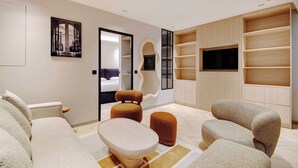 A modern living room with a sofa, ottomans, a coffee table, a TV, and built-in shelving. - Refined Parisian Flat With Designer Finishes - Rue Montorgueil Elegance (Paris)