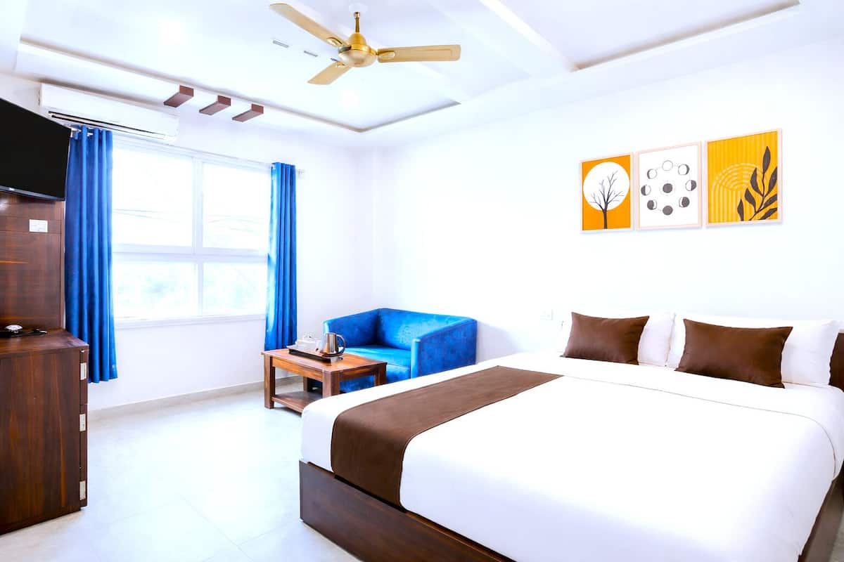 A hotel room with a large bed, a blue armchair, a wooden side table, and a ceiling fan.