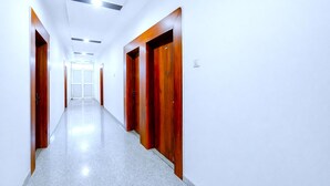 A long, narrow hallway with white walls and a polished floor, leading to a door at the end. - DARWAR PALACE BY AV HOTEL (Bihar Sharif)