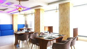 A modern dining area with wooden tables, cushioned chairs, and pendant lighting. - DARWAR PALACE BY AV HOTEL (Bihar Sharif)
