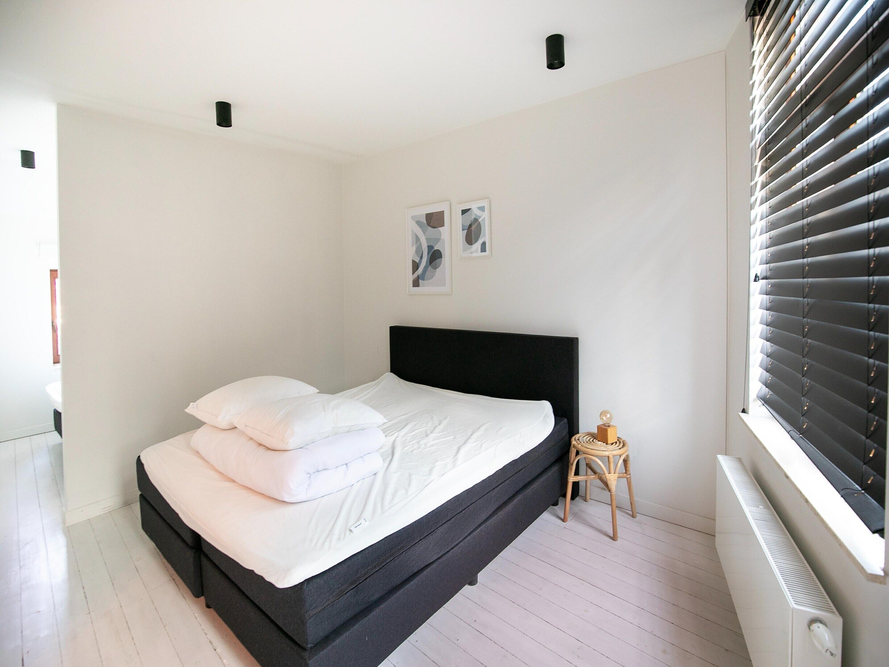 A bedroom with a black bed, white bedding, a small wooden stool, and a radiator.